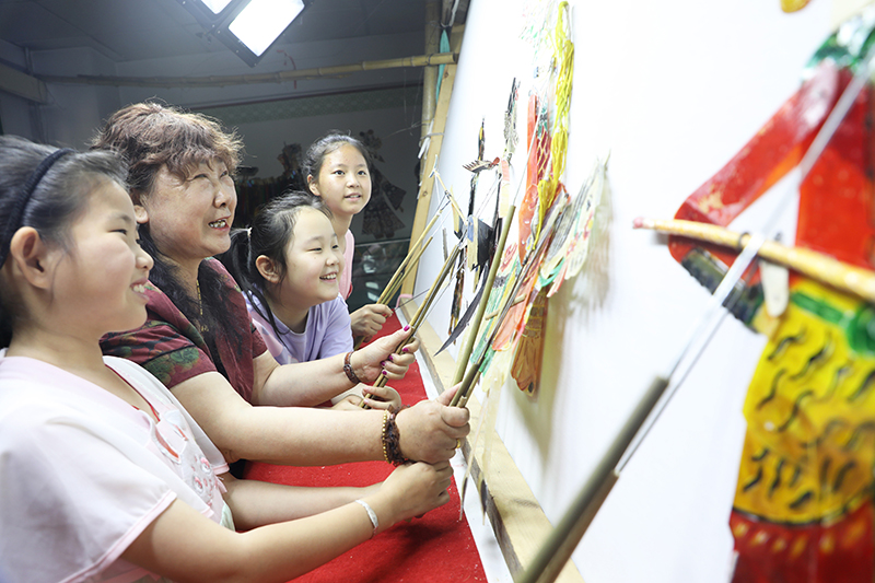 皮影藝人指導(dǎo)小朋友表演皮影戲。